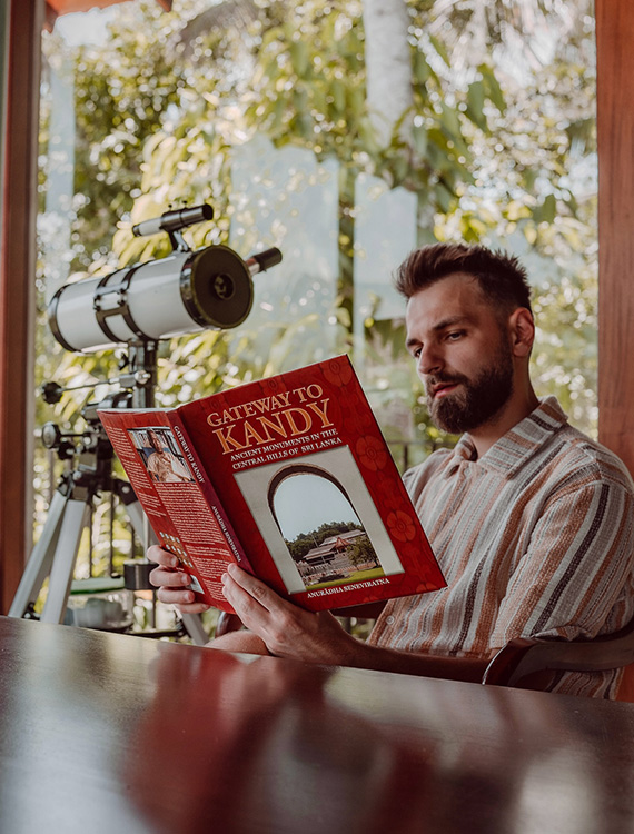 Guest reading a book beside a telescope at Aarunya Nature Resort
