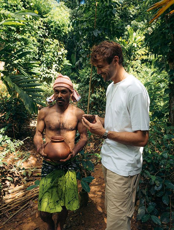 Kithul tapper holding pot while guest smiles with coconut shell of toddy at Aarunya