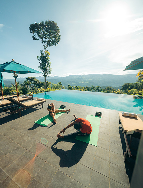 Guest practicing yoga by the pool at Aarunya Nature Resort with scenic views